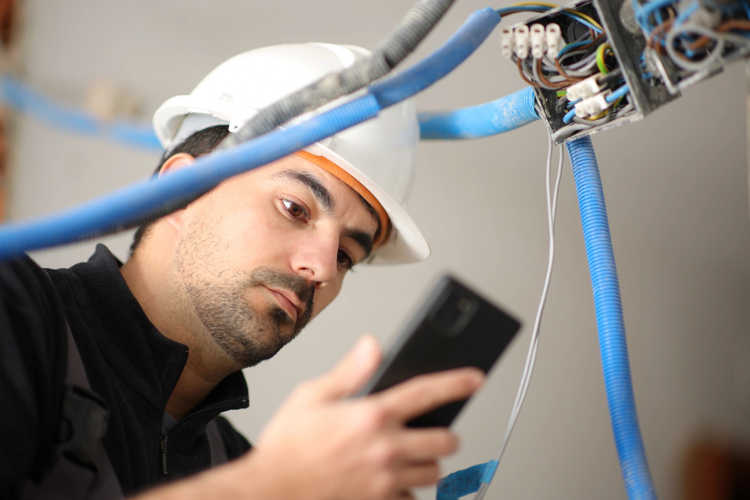 Electrician inspecting electrical wiring with tablet and hard hat